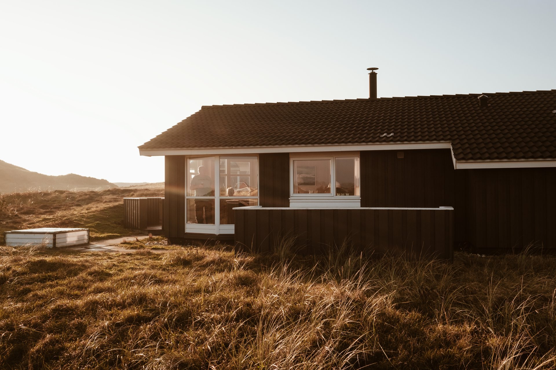 Foto af feriehus i naturen med en person der kigger ud gennem vinduet