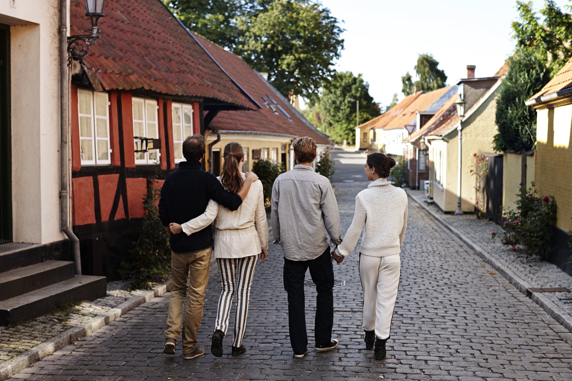 Fire mennesker går ned ad en brostensgade 