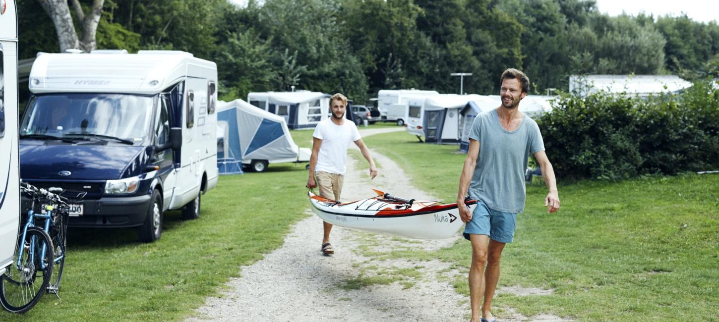To personer bærer en båd gennem en campingplads