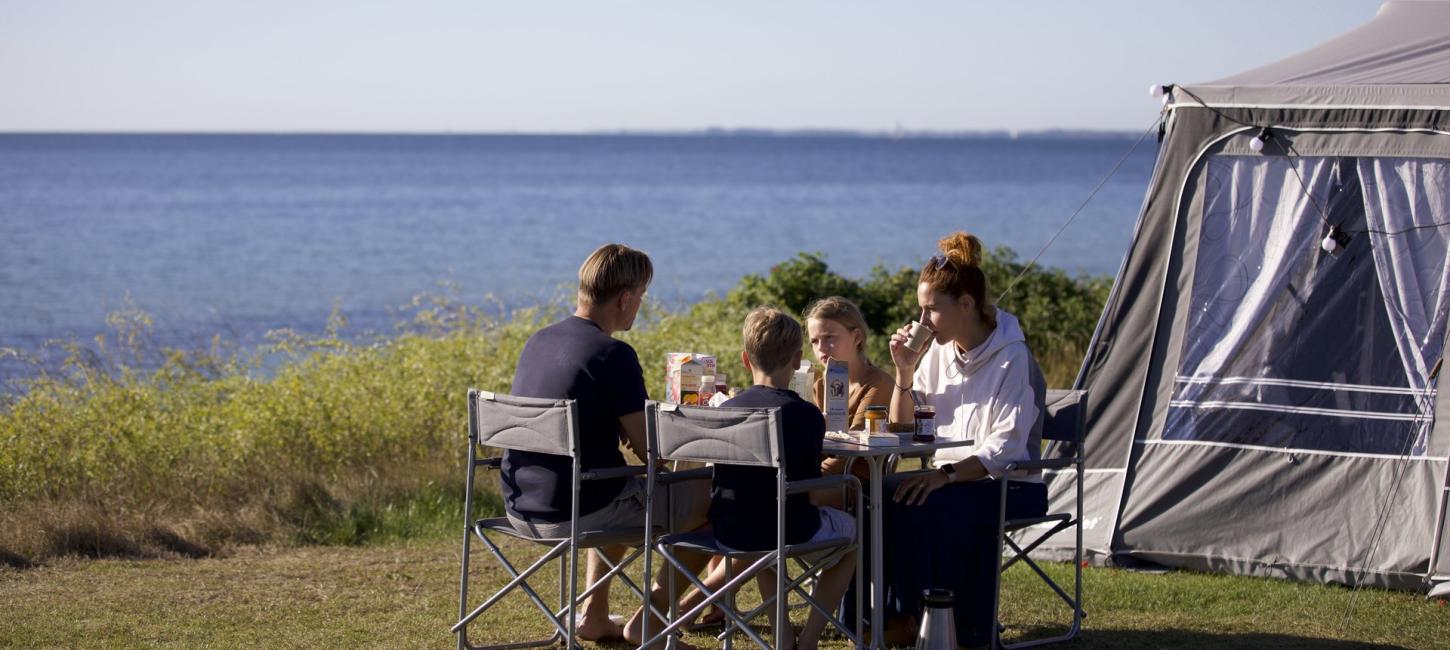 En familie spiser morgenmad på en campingplads med udsigt til vandet