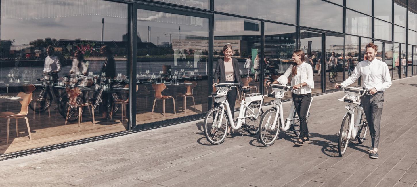 Tre personer i business-tøj trækker sine cykler foran skuespilhuset