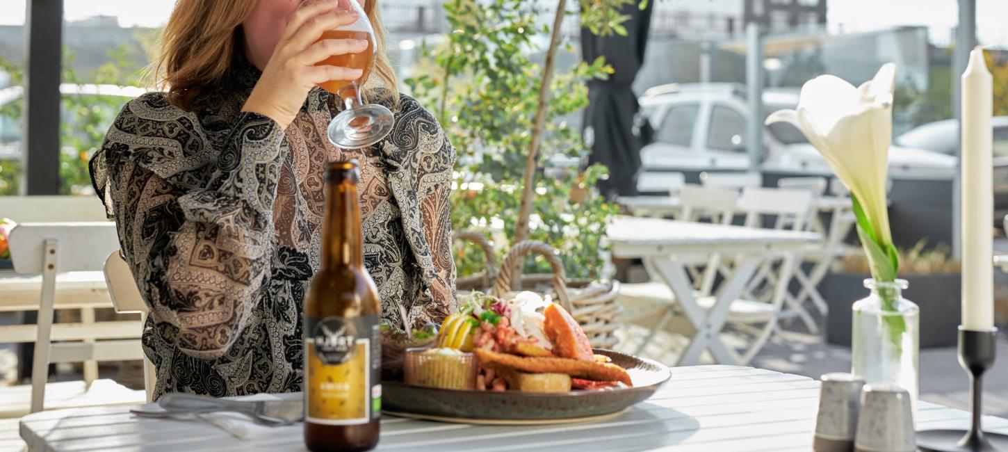 En kvinde nyder en dansk frokost med smørrebrød og øl