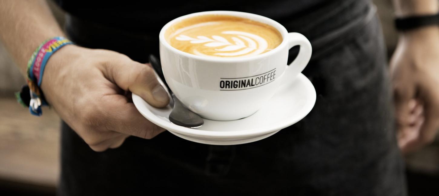 En hånd holder en friskbrygget kop kaffe fra Original Coffee