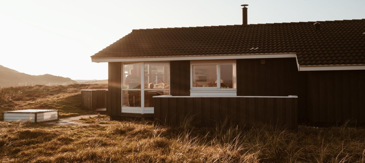 Foto af feriehus i naturen med en person der kigger ud gennem vinduet