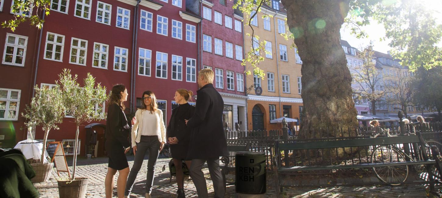 Fire personer taler sammen på Gråbrødretorv i solen.