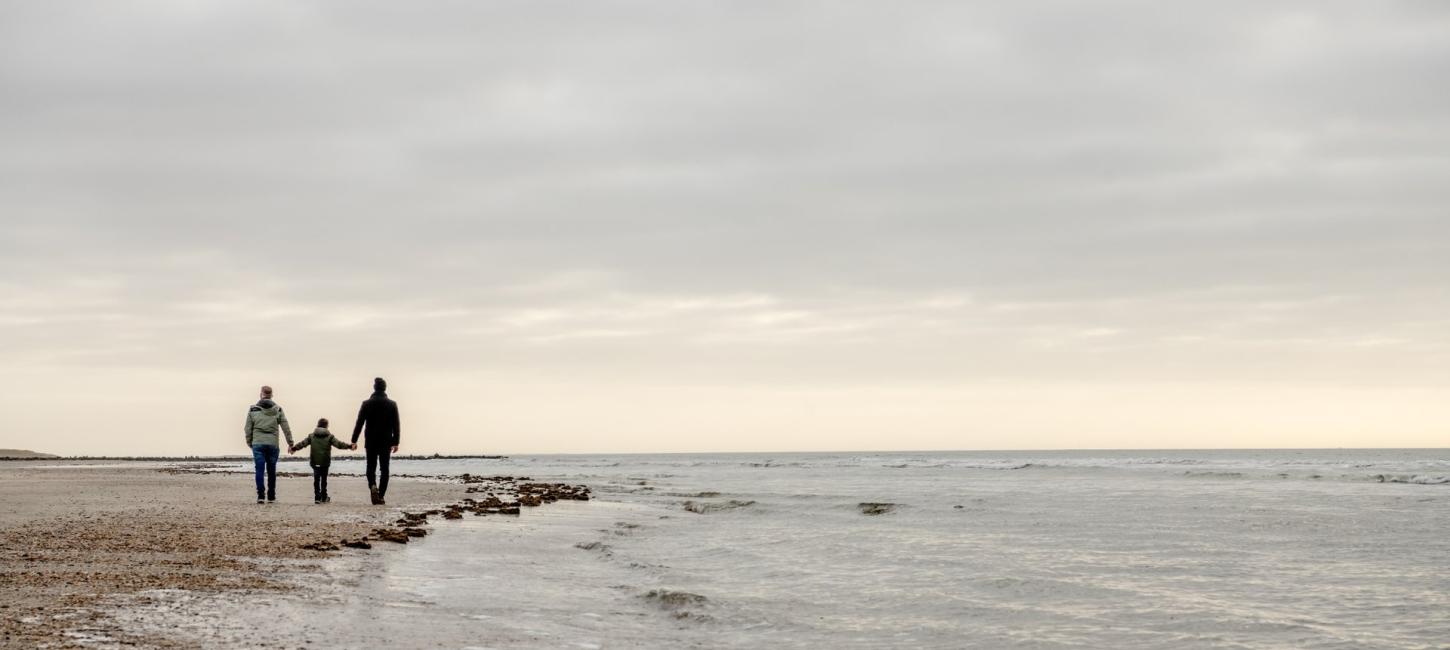 Tre personer går på stranden